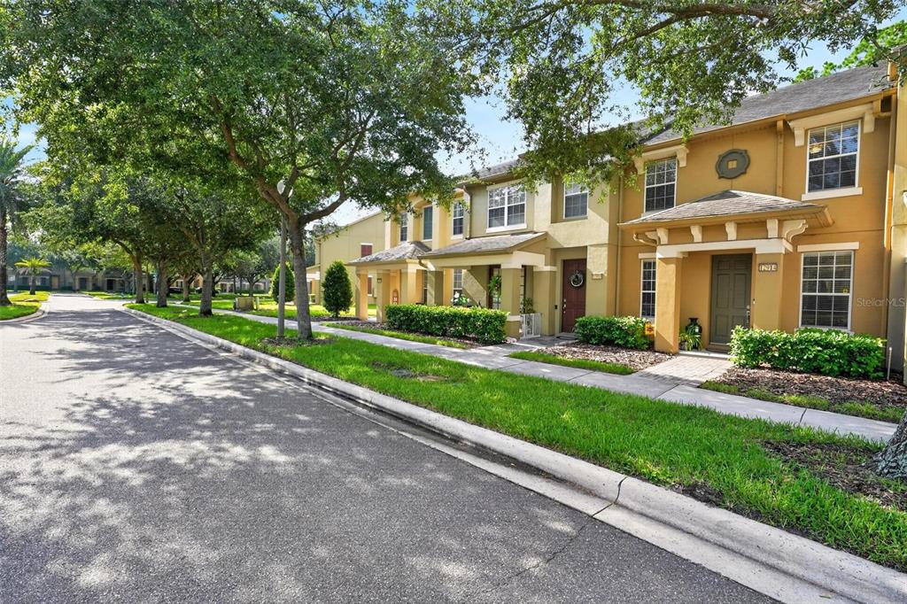 A row of two-story townhomes with yellow stucco exteriors, covered porches, and mature shade trees — 12914 VENNETTA WAY, WINDERMERE, FL