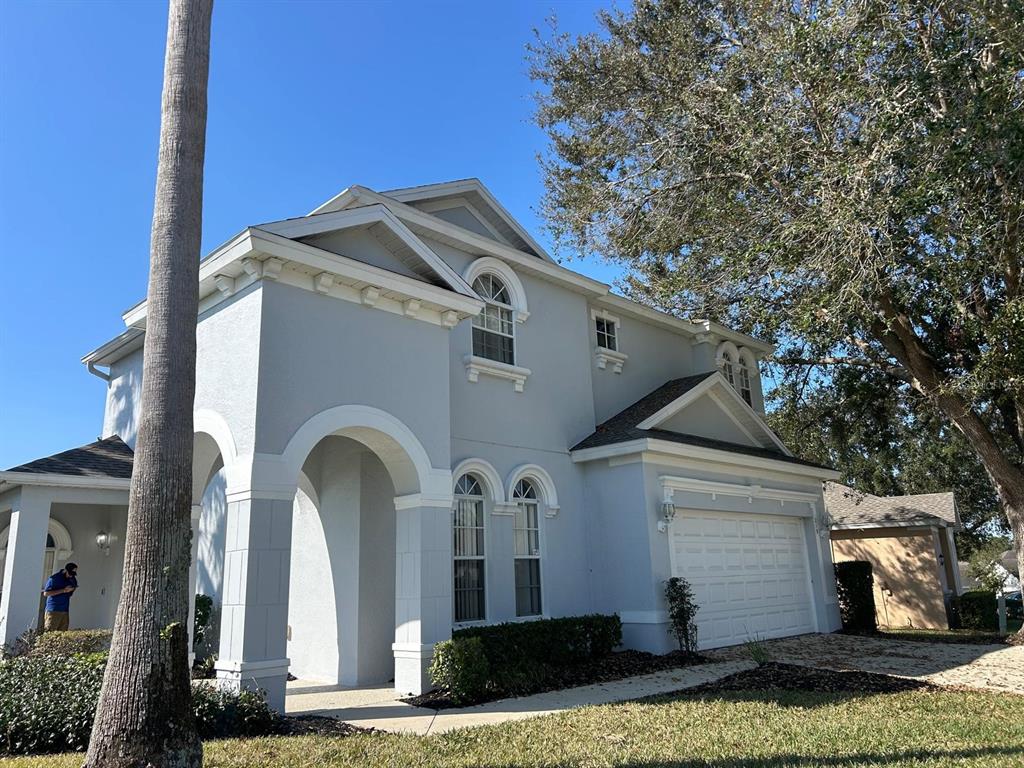 A two-story light gray house with an arched entryway, a garage, and a palm tree — 219 PLUMOSO LOOP, DAVENPORT, FL