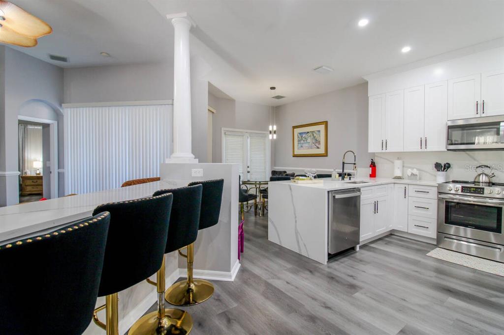 A modern kitchen features white cabinets, a marble-topped island, and black bar stools — 219 PLUMOSO LOOP, DAVENPORT, FL