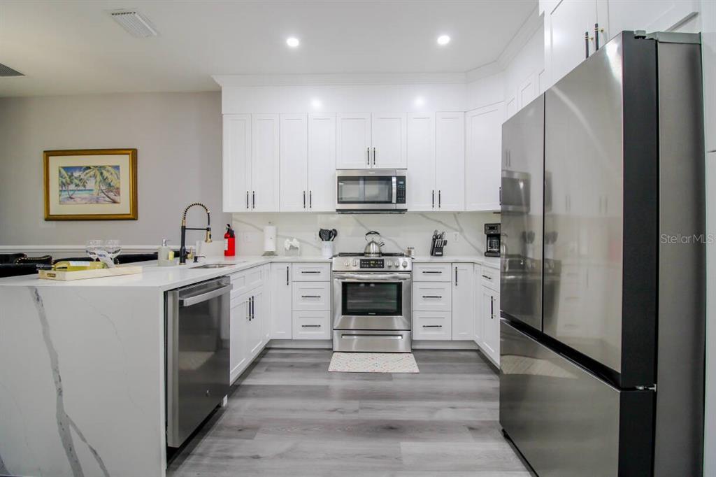 A modern kitchen features white cabinetry, stainless steel appliances, and a marble-topped island — 219 PLUMOSO LOOP, DAVENPORT, FL