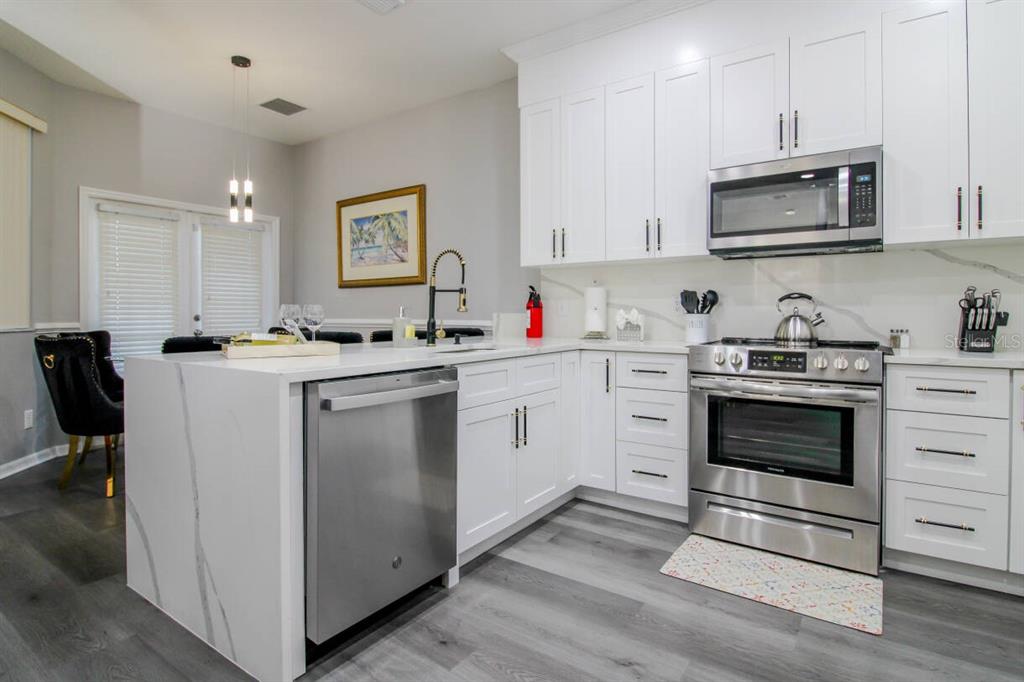A modern kitchen features white cabinets, stainless steel appliances, and a quartz waterfall island — 219 PLUMOSO LOOP, DAVENPORT, FL