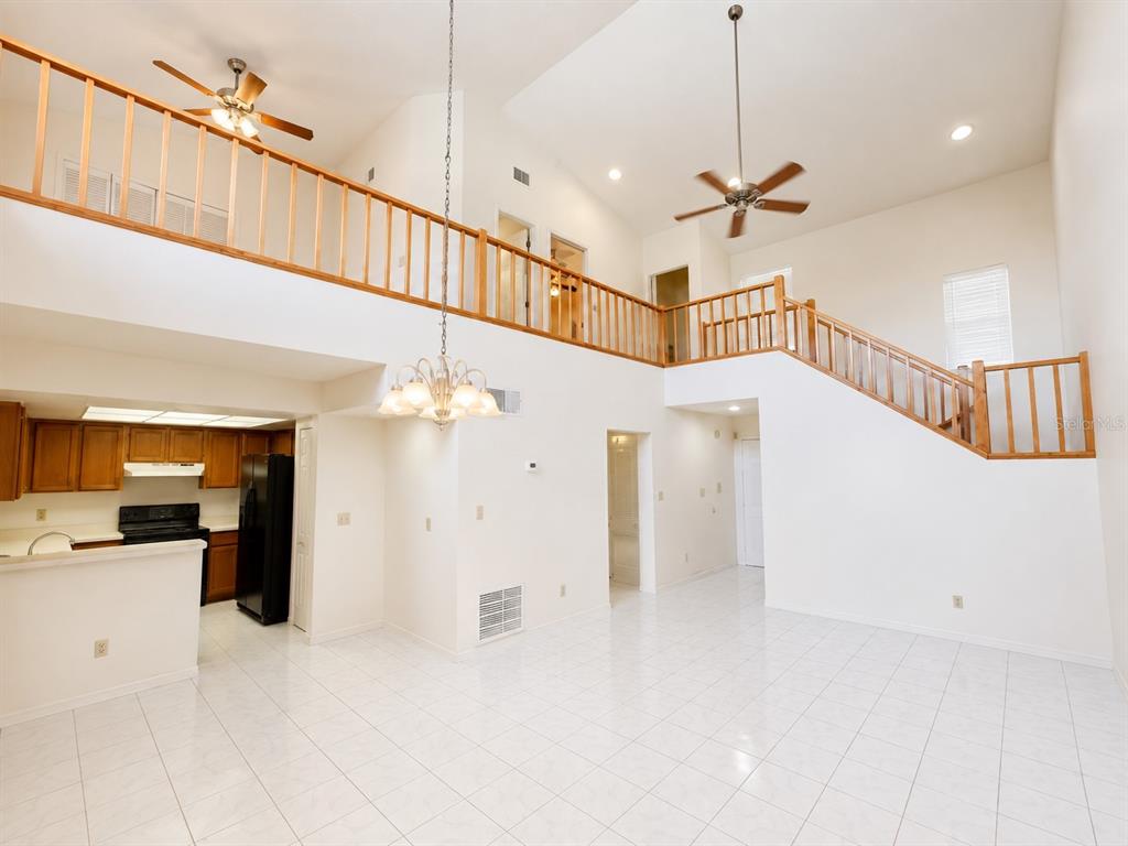 A high-ceilinged living area with white tile floors, a wooden balcony, and an adjacent kitchen — 4011 AUGUST COURT, CASSELBERRY, FL