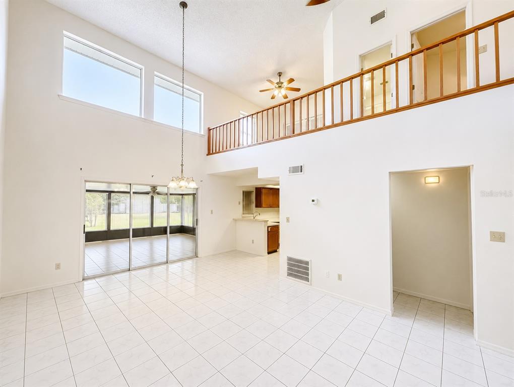 A bright, high-ceilinged living area features white tile flooring, a wooden loft railing, and kitchen — 4011 AUGUST COURT, CASSELBERRY, FL
