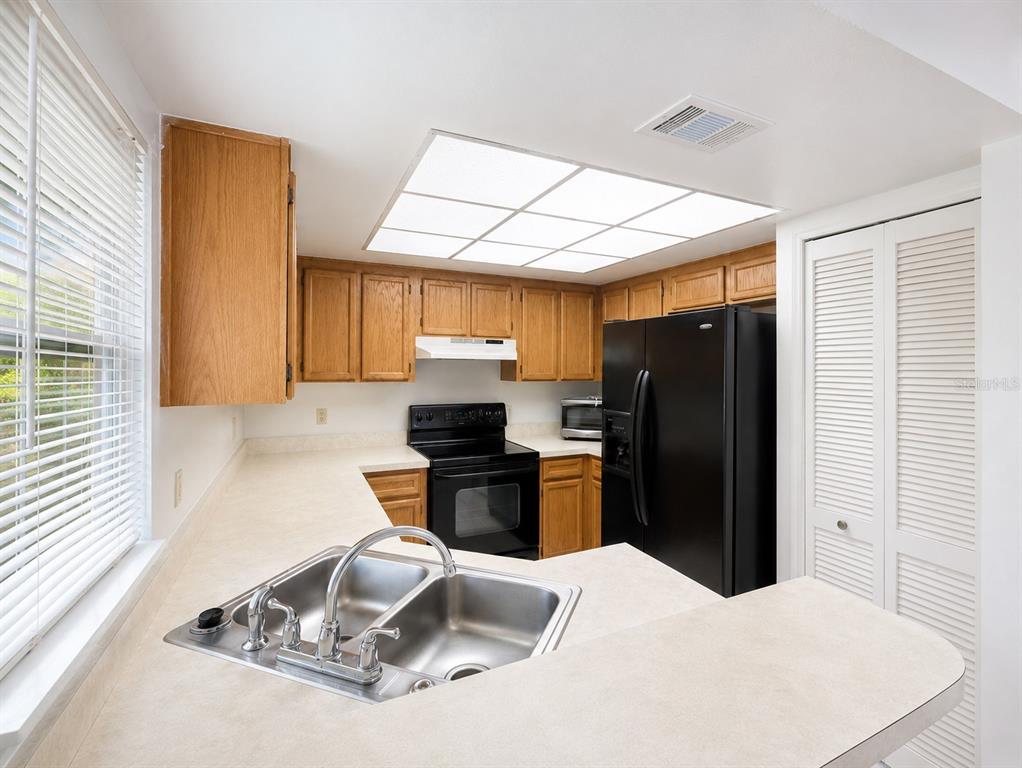 A kitchen features oak cabinets, black appliances, a double sink, and a drop ceiling light — 4011 AUGUST COURT, CASSELBERRY, FL