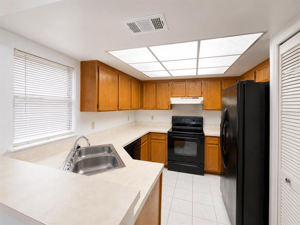 A kitchen features wood cabinets, beige countertops, a black stove, and a black refrigerator — 4011 AUGUST COURT, CASSELBERRY, FL