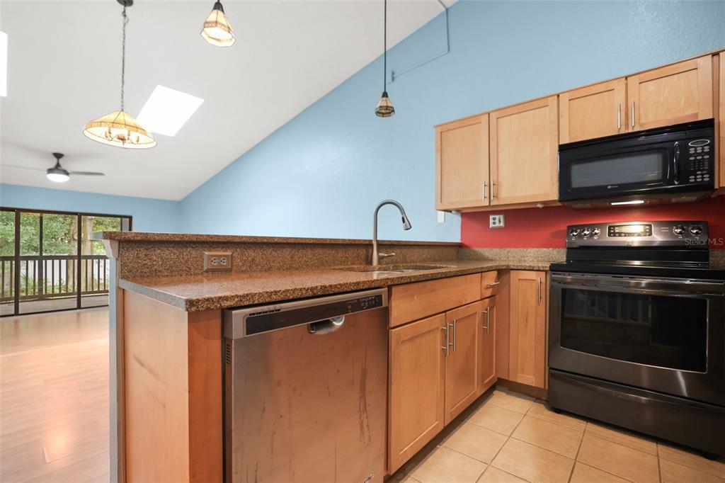 A kitchen with light wood cabinets, granite countertops, stainless steel appliances, and blue walls — 6436 92ND PLACE N UNIT 1004, PINELLAS PARK, FL