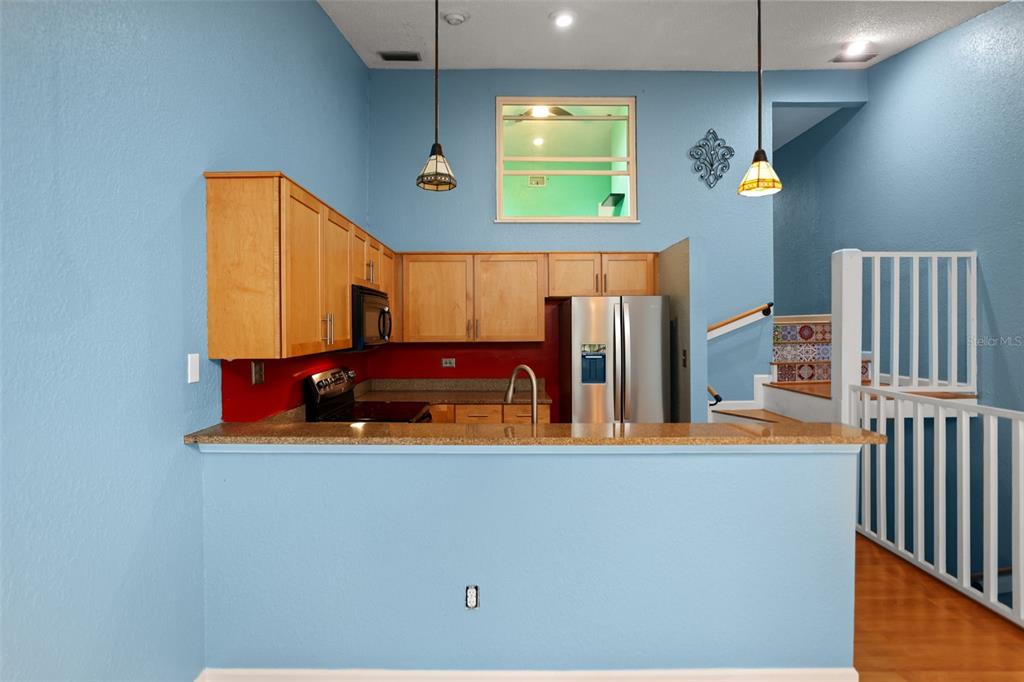 A kitchen with light blue walls, wood cabinets, a granite countertop, and a breakfast bar — 6436 92ND PLACE N UNIT 1004, PINELLAS PARK, FL