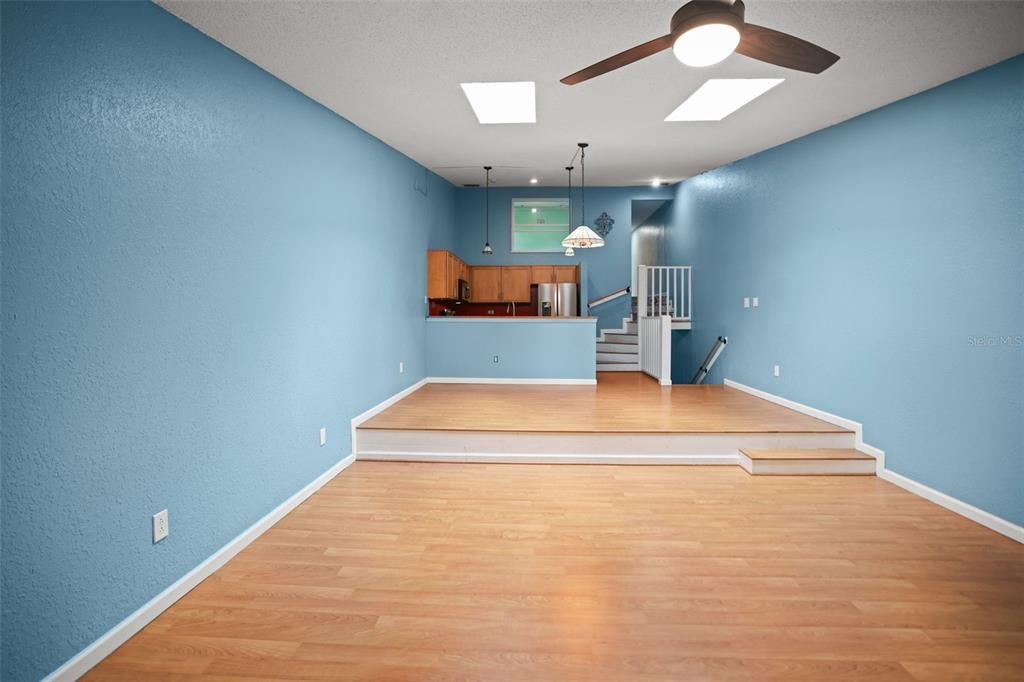 A living area with light wood flooring leads up to a kitchen on a raised platform — 6436 92ND PLACE N UNIT 1004, PINELLAS PARK, FL