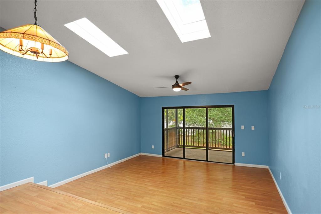 A living room with blue walls, wood-look flooring, a ceiling fan, and sliding glass doors — 6436 92ND PLACE N UNIT 1004, PINELLAS PARK, FL