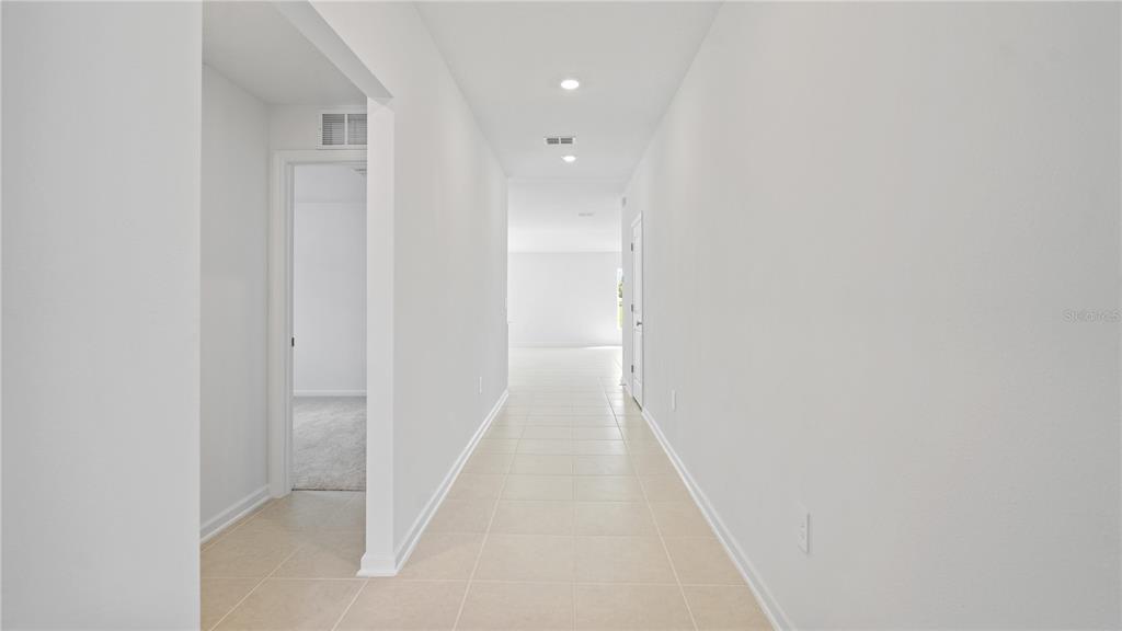 A long, white-walled hallway with light-colored tile flooring leads toward an open living area — 1933 PINE MEADOWS GOLFCOURSE ROAD, EUSTIS, FL