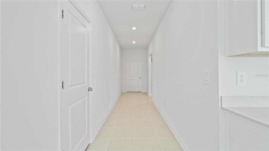 A narrow hallway with white walls, tile flooring, and a door at the far end — 1933 PINE MEADOWS GOLFCOURSE ROAD, EUSTIS, FL