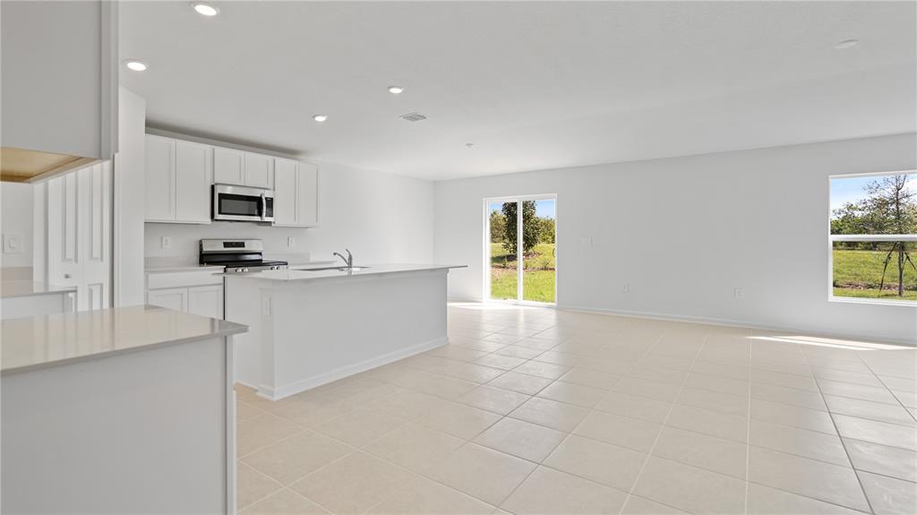 A kitchen with white cabinets and an island opens into a spacious, tiled living area — 1933 PINE MEADOWS GOLFCOURSE ROAD, EUSTIS, FL