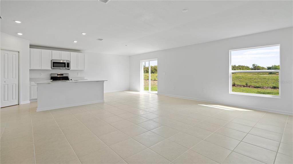 An open-concept kitchen and living area features white cabinetry, tile flooring, and a sliding door — 1933 PINE MEADOWS GOLFCOURSE ROAD, EUSTIS, FL