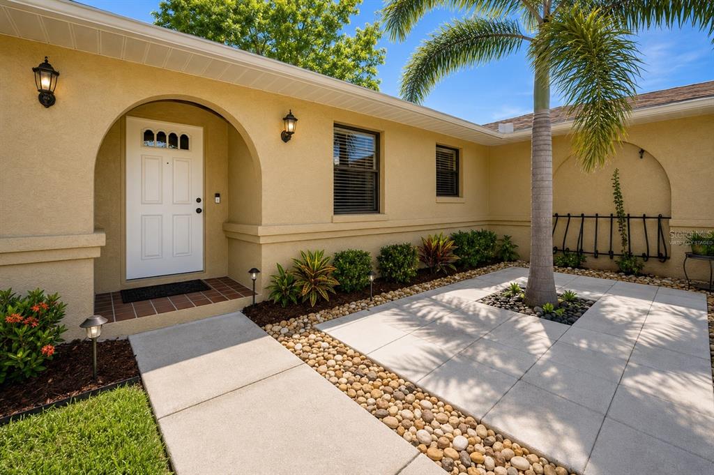 A beige stucco house exterior features an arched entryway, a palm tree, and stone landscaping — 3011 SHADOW OAKS DRIVE, HOLIDAY, FL
