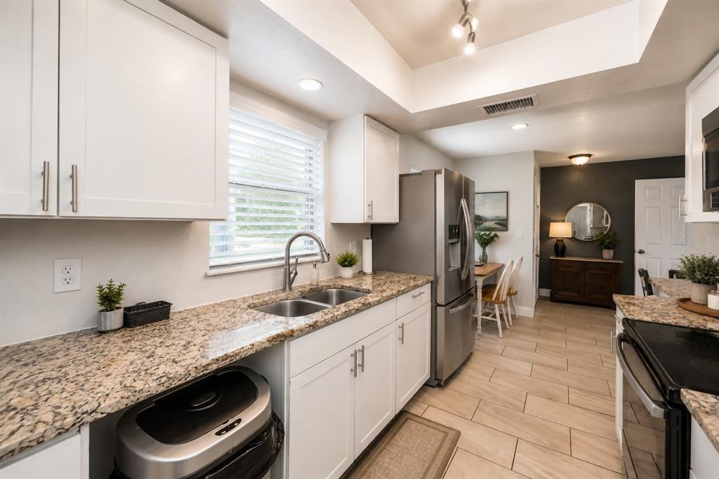 A kitchen with white cabinets, granite countertops, stainless steel appliances, and tile flooring — 3011 SHADOW OAKS DRIVE, HOLIDAY, FL