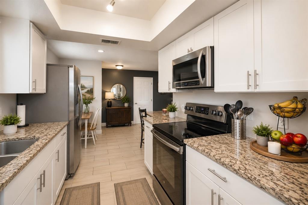 A kitchen with white cabinets, granite countertops, stainless steel appliances, and light tile flooring — 3011 SHADOW OAKS DRIVE, HOLIDAY, FL