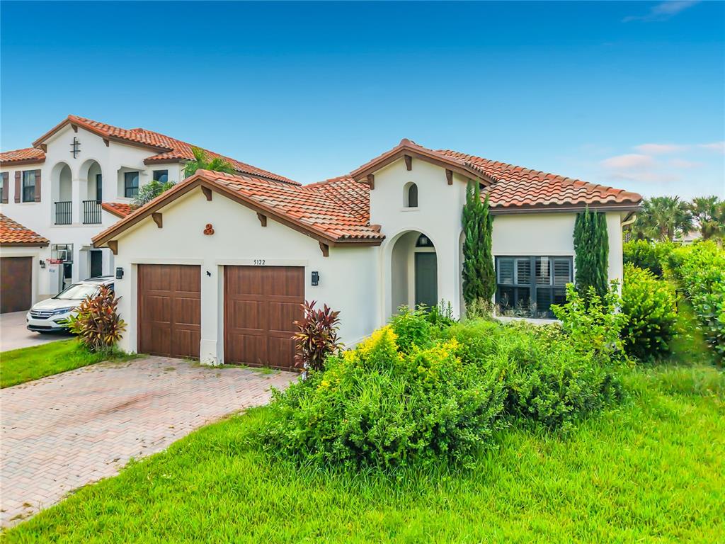 A single-story house with a terracotta tile roof, two garage doors, and a paved driveway — 5122 MONZA COURT, AVE MARIA, FL