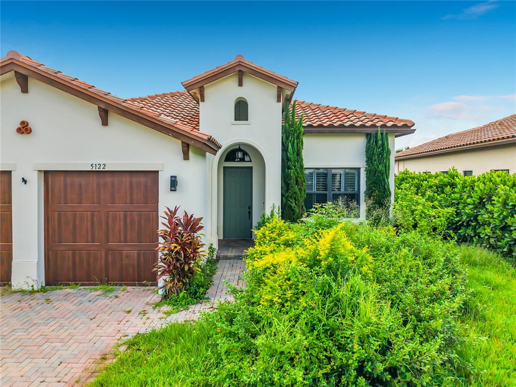A single-story house with a brown garage door, arched entryway, and a tiled roof — 5122 MONZA COURT, AVE MARIA, FL