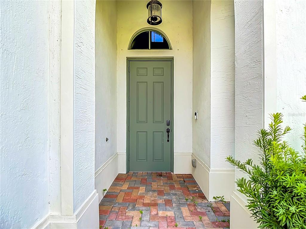 A sage green front door sits under a semi-circular transom window on a brick porch — 5122 MONZA COURT, AVE MARIA, FL