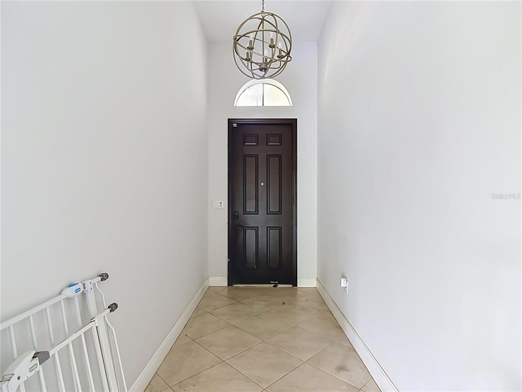 A narrow entryway features a dark front door, a spherical chandelier, and light-colored tile flooring — 5122 MONZA COURT, AVE MARIA, FL