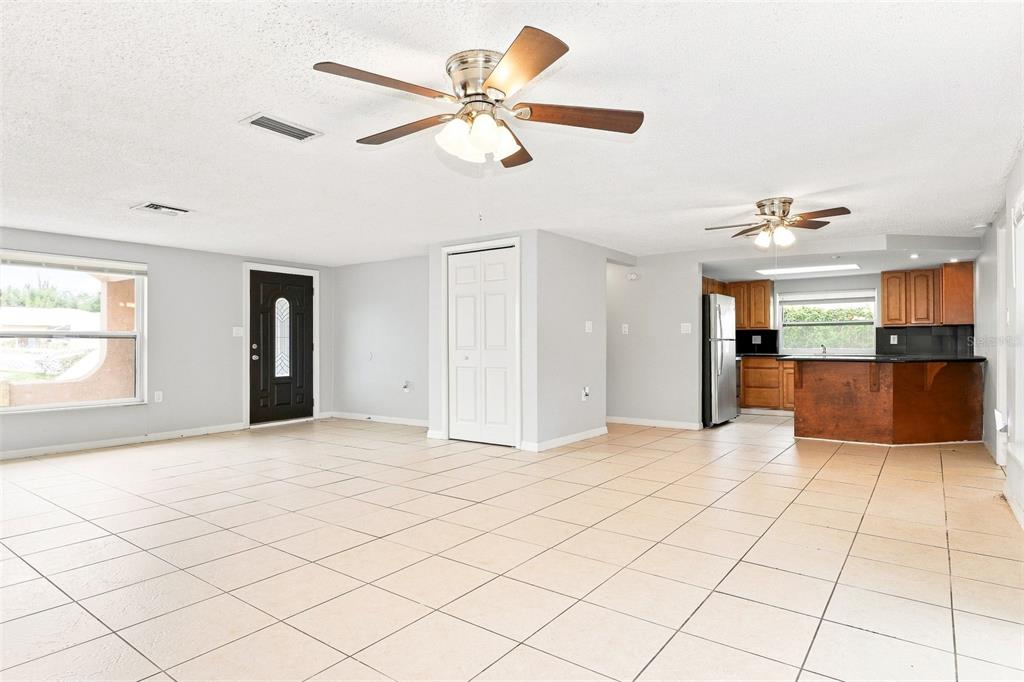 An open-concept living room with tile flooring, two ceiling fans, and an adjacent kitchen — 7235 WESTWIND DRIVE, PORT RICHEY, FL