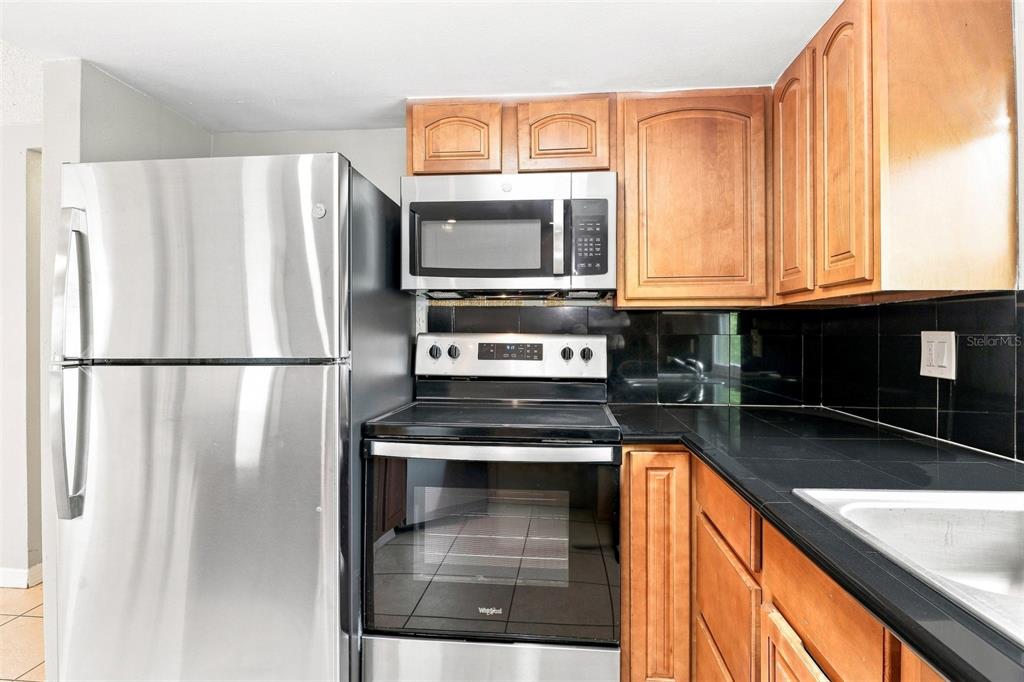 A kitchen features stainless steel appliances, wood cabinets, and black tile countertops and backsplash — 7235 WESTWIND DRIVE, PORT RICHEY, FL