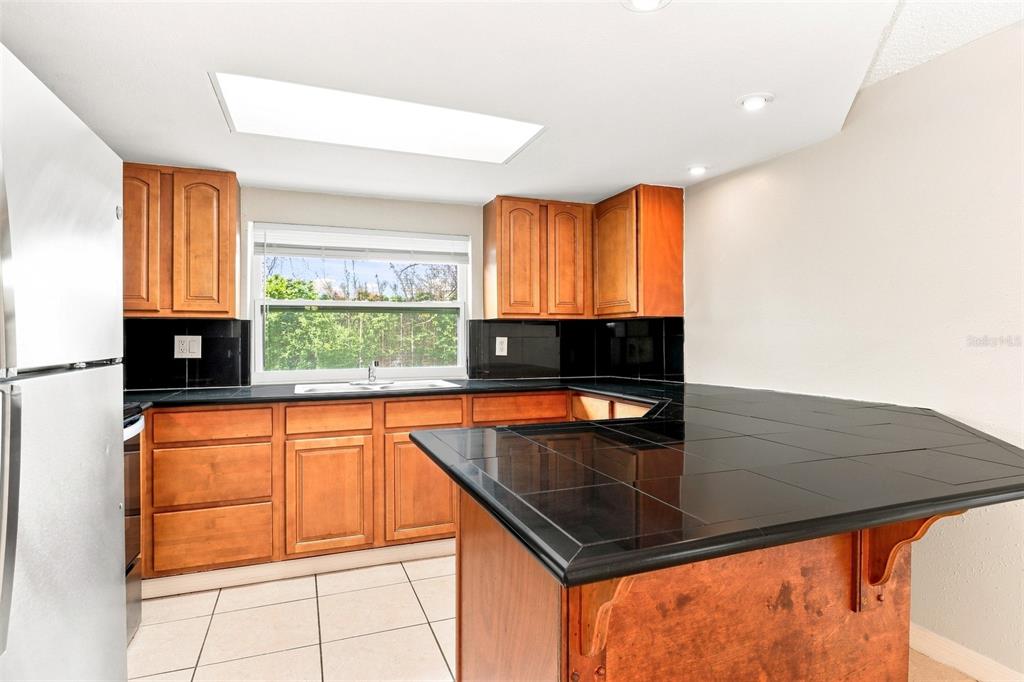 A kitchen with wooden cabinets, black tile countertops, a window, and a skylight — 7235 WESTWIND DRIVE, PORT RICHEY, FL