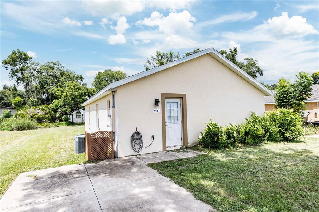 A side view of a small, light-colored house with a concrete driveway and a white door — 3534 COUNTY ROAD 230C, WILDWOOD, FL