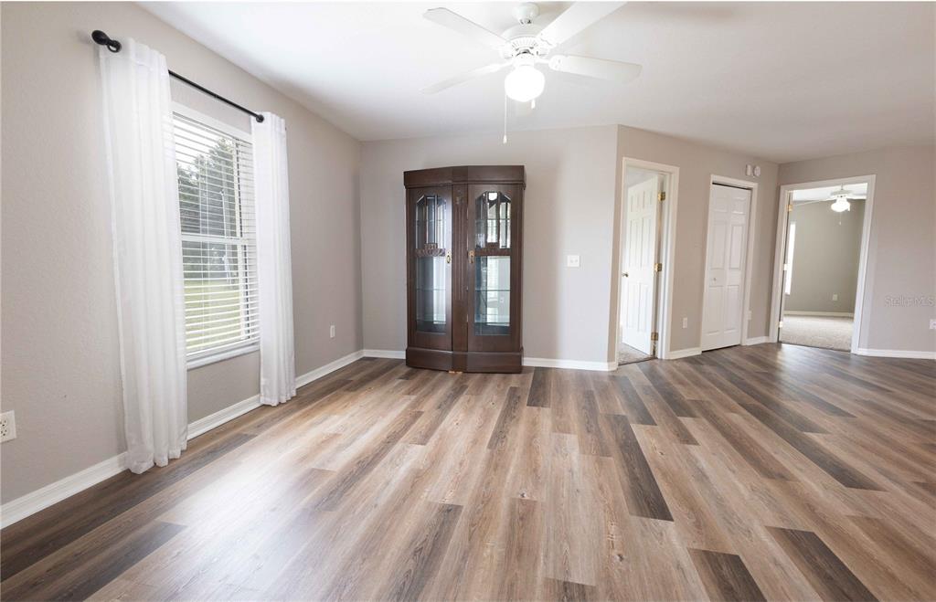 A room with wood-look flooring, a ceiling fan, a corner curio cabinet, and white curtains — 3534 COUNTY ROAD 230C, WILDWOOD, FL