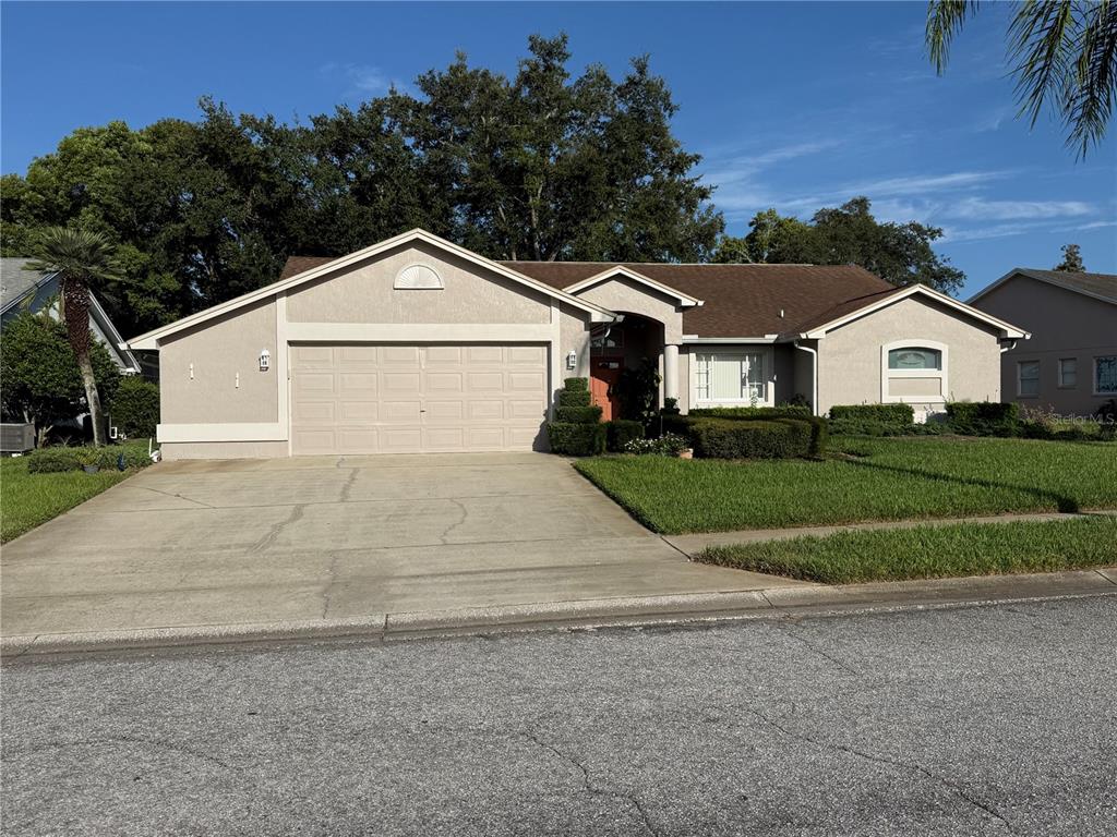 A single-story suburban house with a beige stucco exterior, a two-car garage, and a lawn — 13928 TENNYSON DRIVE, HUDSON, FL