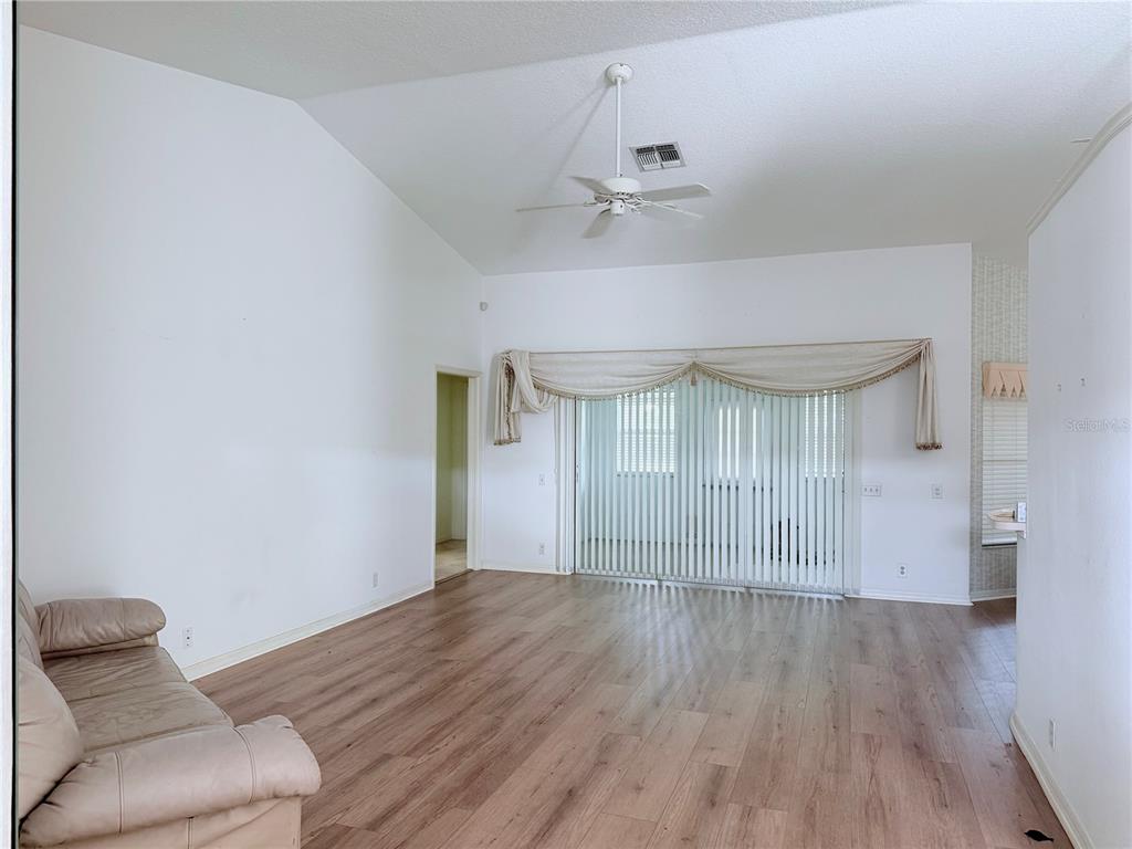 A living room with wood-look flooring, a vaulted ceiling, a ceiling fan, and sliding doors — 13928 TENNYSON DRIVE, HUDSON, FL