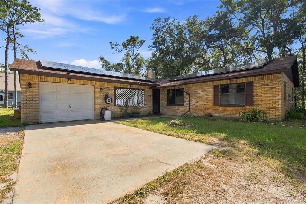A single-story brick house with a solar panel roof, a garage, and a concrete driveway — 7059 JUNIPER AVENUE, WEBSTER, FL