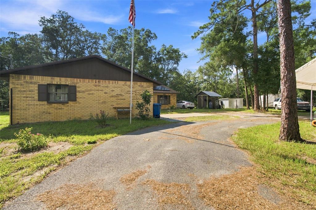 A yellow brick house with a driveway and a flagpole stands among trees — 7059 JUNIPER AVENUE, WEBSTER, FL