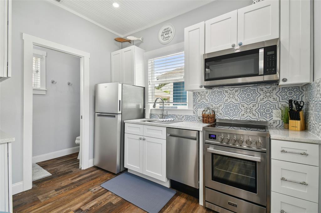 A kitchen features white cabinets, stainless steel appliances, and a patterned blue and white backsplash — 602 1/2 SKINNER BOULEVARD, DUNEDIN, FL