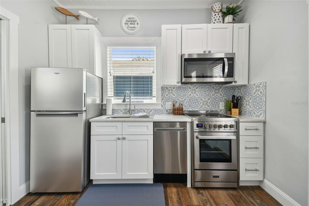 A small kitchen features white cabinets, stainless steel appliances, and a blue patterned tile backsplash — 602 1/2 SKINNER BOULEVARD, DUNEDIN, FL