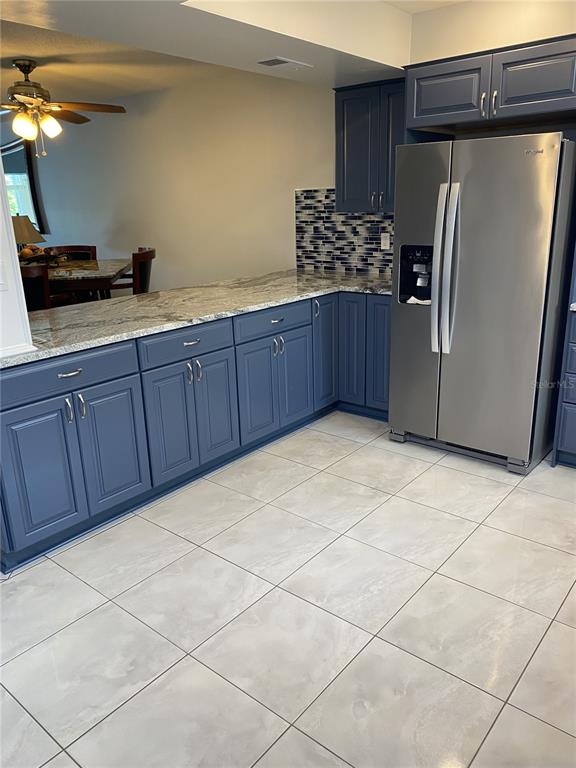 A kitchen features blue cabinets, granite countertops, a stainless steel refrigerator, and tiled flooring — 5555 GULF BOULEVARD UNIT 104, ST PETE BEACH, FL