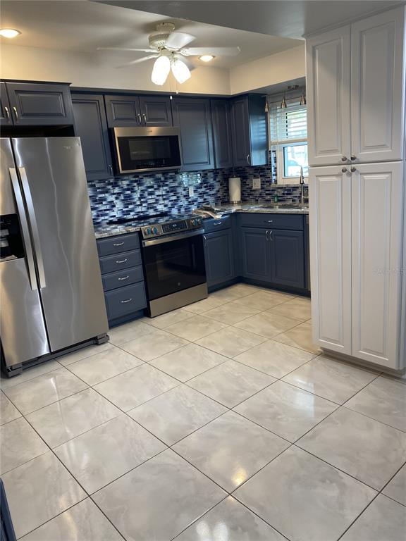 A kitchen features blue cabinets, stainless steel appliances, a tiled backsplash, and white floor tiles — 5555 GULF BOULEVARD UNIT 104, ST PETE BEACH, FL