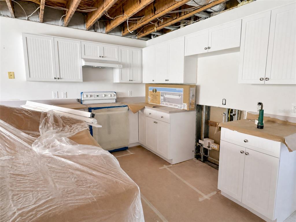 An unfinished kitchen features white cabinets, a stove, and exposed ceiling joists — 6800 PLACIDA ROAD UNIT TH-3D, ENGLEWOOD, FL