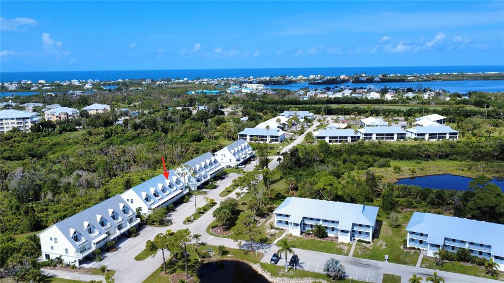 An aerial view shows multi-story residential buildings with metal roofs surrounded by lush vegetation — 6800 PLACIDA ROAD UNIT TH-3D, ENGLEWOOD, FL