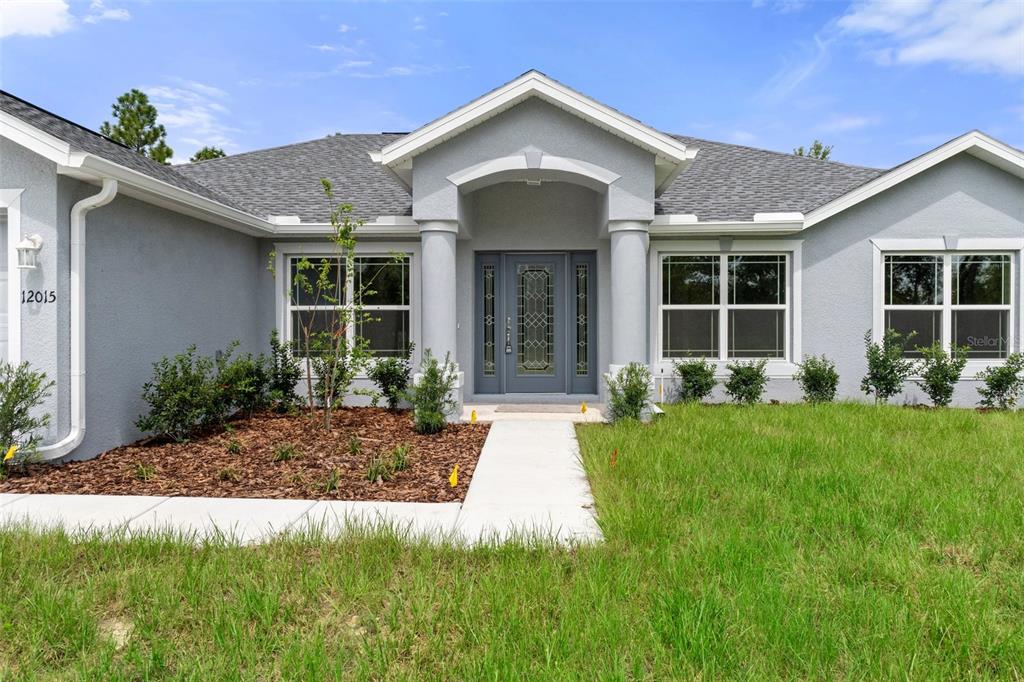 A gray single-story house features a covered entryway with columns and a decorative glass door — 12085 MANASSAS AVENUE, WEEKI WACHEE, FL