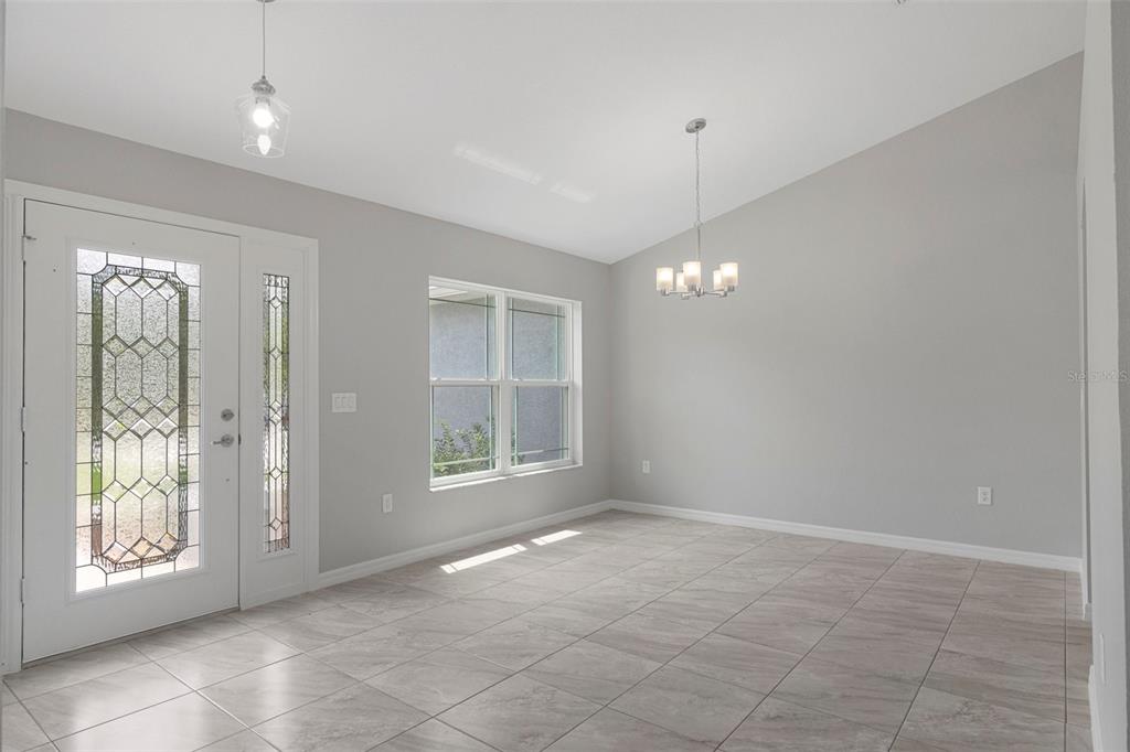 An empty room with light gray walls, tile flooring, a vaulted ceiling, and a chandelier — 12085 MANASSAS AVENUE, WEEKI WACHEE, FL