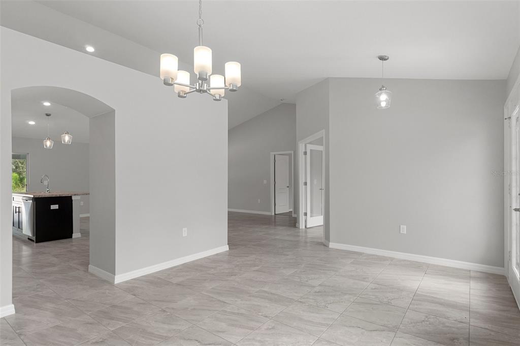A bright, open-concept dining area features light gray walls, tile flooring, and a modern chandelier — 12085 MANASSAS AVENUE, WEEKI WACHEE, FL
