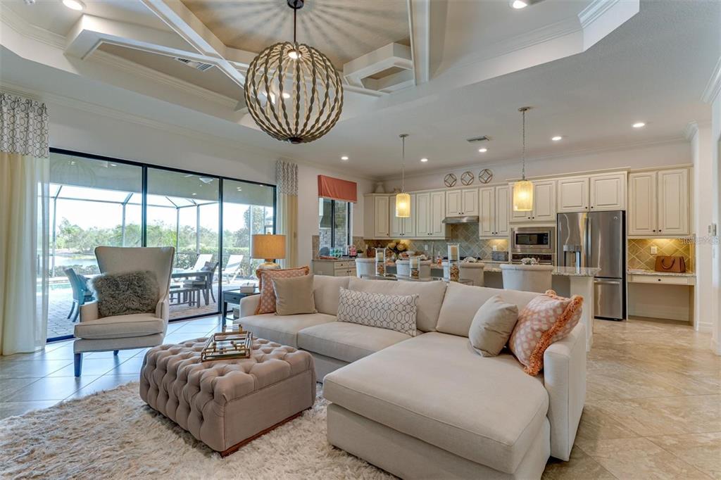 An open-concept living room and kitchen featuring a large sectional, tufted ottoman, and sliding doors — 5803 CESSNA RUN, BRADENTON, FL