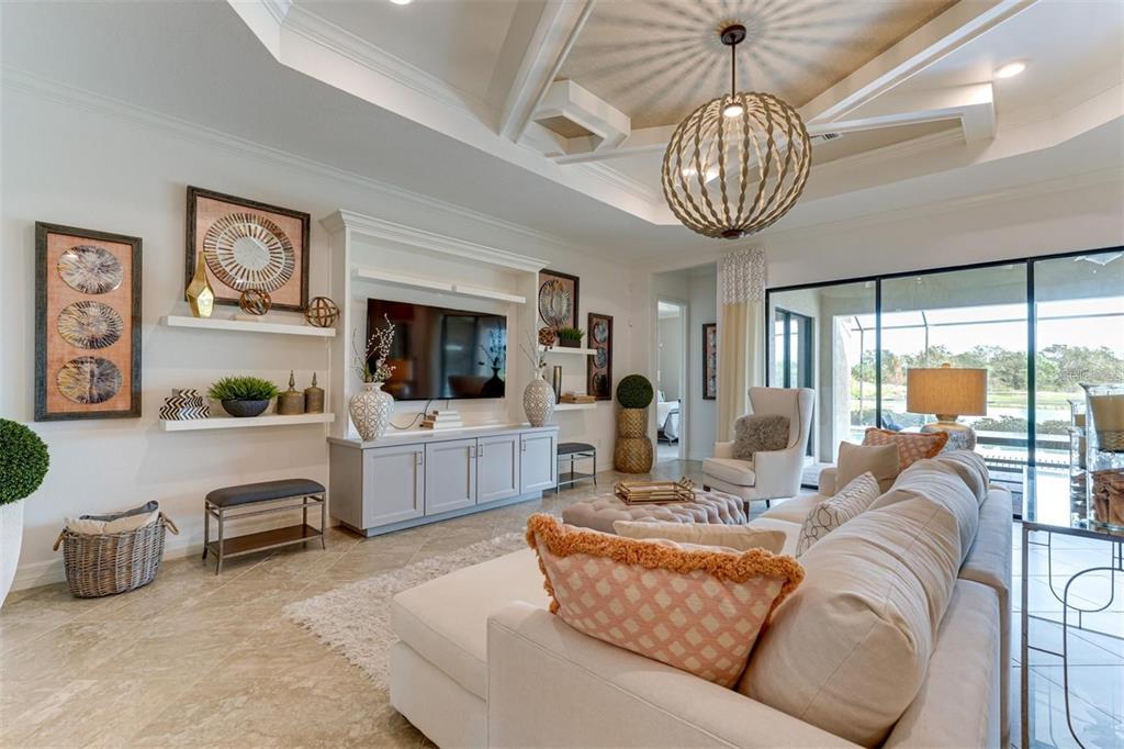 A bright living room features a tray ceiling, a large sectional sofa, and built-in cabinetry — 5803 CESSNA RUN, BRADENTON, FL