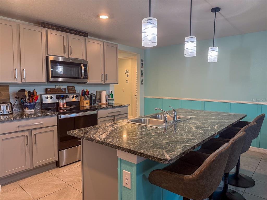 A kitchen features gray cabinets, a granite-topped island with a sink, and light blue walls — 4120 QUIET RAIN COURT, PALMETTO, FL