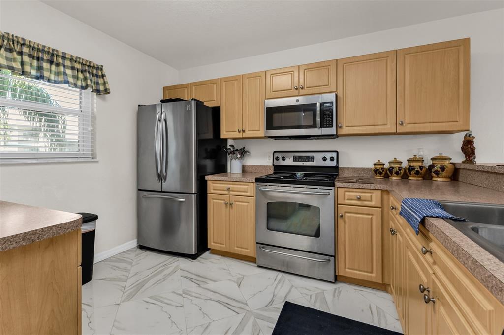 A kitchen features light wood cabinets, stainless steel appliances, and white marble-patterned tile flooring — 175 KINGS HIGHWAY UNIT #227-B7, PUNTA GORDA, FL