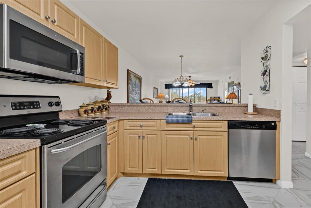 A kitchen with light wood cabinets, stainless steel appliances, and a view into the living area — 175 KINGS HIGHWAY UNIT #227-B7, PUNTA GORDA, FL