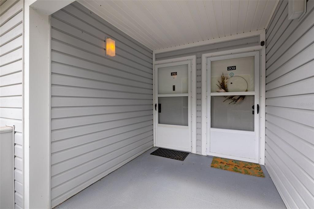 An exterior view of a covered entryway featuring two white doors numbered 209 and 210 — 210 RIVER BEND PLACE UNIT B, WELAKA, FL