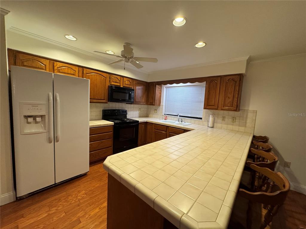 A kitchen features oak cabinets, a black stove and microwave, and white tile countertops — 10 FORT CLINCH HEIGHTS ROAD, FROSTPROOF, FL