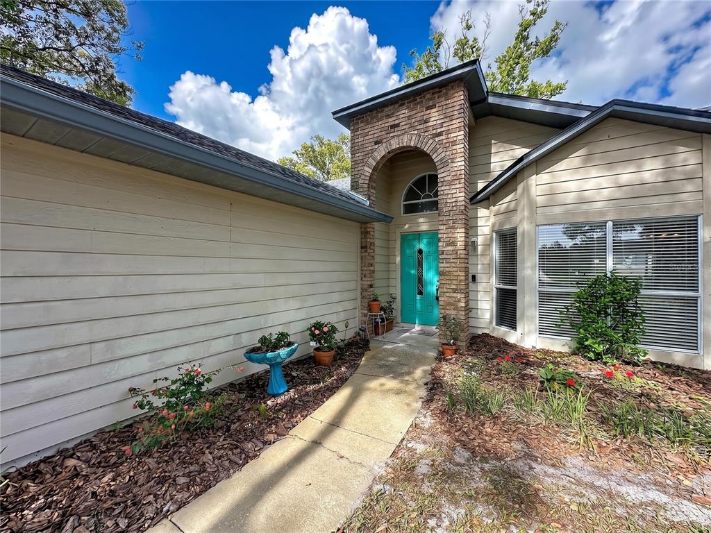 A beige house exterior features a brick entryway arch and a bright teal front door — 1681 E SPRING RIDGE CIRCLE, WINTER GARDEN, FL
